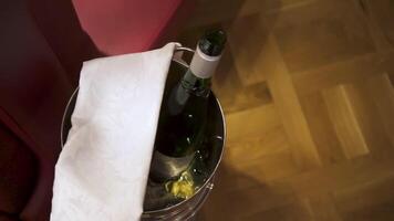 bottiglia di Champagne nel benna. azione filmato. superiore Visualizza di ghiaccio secchio con un ha aperto bottiglia di alcolizzato bevanda e bianca stoffa in piedi su il pavimento. video