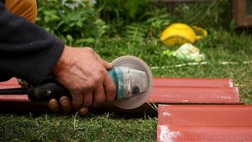 Roofer using an angle grinder machine to cut a roof tile of red color. Stock footage. Close up of male worker hands cutting a roof tile with a professional saw. video