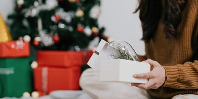 Close up woman opening present near Christmas tree. Happy holidays and New Year. photo