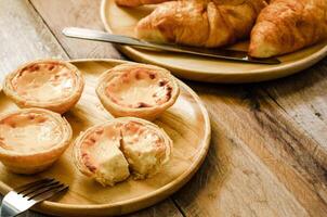 Egg tarts and croissants on a wooden plate on a wooden table. photo