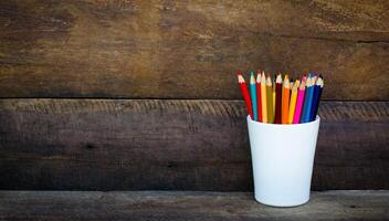 Stack of colored pencils in a glass on wooden background photo