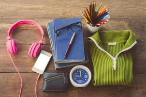 Accessories, sweaters, books, pens, glasses, colored pencils, clocks, smart phones, put on a wooden table photo