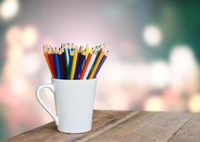 colored pencils in a glass on wooden background light bokeh photo