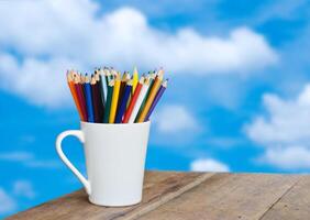 de colores lapices en un vaso en de madera antecedentes nubes en el cielo foto