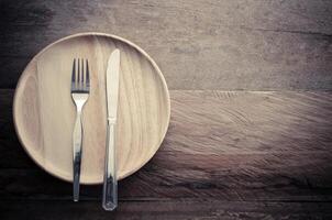 Knife and fork on wood plate placed on a wooden table - still life. photo