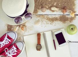 Travel accessories, hats, sunglasses, notebook, pen, phone, shell, placed on a wooden floor photo