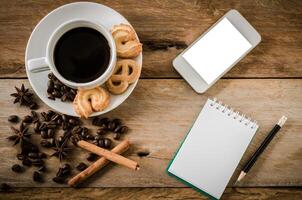 café galletas y teléfono inteligente cuaderno en un de madera mesa en el Mañana. foto