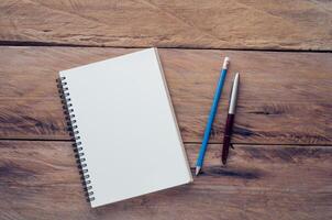 blank notebook with pencil and pen on wooden table - still life photo