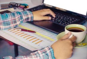 Businessman at work. Close-up top view of man working on laptop and data  while sitting at the wooden desk photo