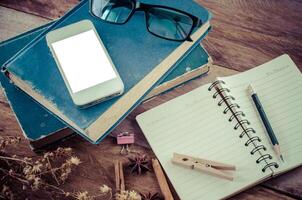 smartphone is on a book Include pencil is on a notebook ,eyeglasses on the wooden background. photo