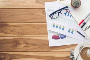 coffee cup, chart, pen, notebook and accessory for work on wooden table. photo