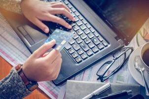 View of male hands holding credit card numbers typed on the computer keyboard while sitting at a desk - focus hand. photo