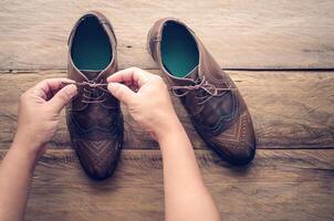 Hands of a young man shoelace on wooden floor photo