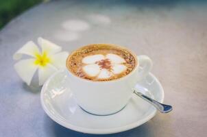 A cup of coffee plumeria pattern in a white cup on wooden background photo