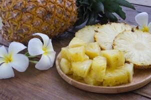 Sliced pineapple on wooden plate decorated with beautiful flowers. photo