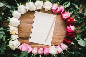 Colorful roses lined up on a wooden floor paper and pencil with space for writing your message. photo