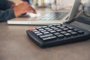 The calculator is placed on an office table with a laptop and the team is working behind the scenes. photo