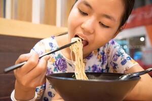 Asian girl is eating noodles with chopsticks. photo