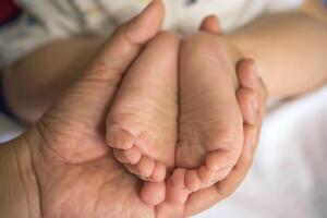 el manos de el madre sostener el del bebe pies con amor y cariñoso. foto