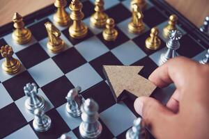 The hand of a businessman who is holding an arrow icon to point the target at strategic placement in the chess table - a guiding concept in business. photo