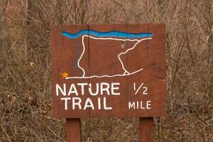 This sign in the woods marks the area of the trail. Helping to keep hikers from getting them lost and leading the way. The brown paint looks worn and chipping. The white letters standing out. photo