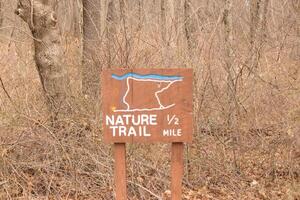 This sign in the woods marks the area of the trail. Helping to keep hikers from getting them lost and leading the way. The brown paint looks worn and chipping. The white letters standing out. photo