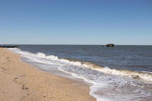 I loved the look of this beach as the waves battered the shore. The whitecaps of the waves make it look rough. The beautiful blue sky with no clouds in site make this look like a beautiful summer day. photo