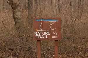 This sign in the woods marks the area of the trail. Helping to keep hikers from getting them lost and leading the way. The brown paint looks worn and chipping. The white letters standing out. photo