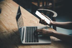 mockup image of a woman's hand working on a laptop and smart phone with blank white desktop copy space screen on a desk photo