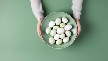 AI generated Two hands holding a light green plate filled with pale-hued eggs against a green background, suitable for Easter and spring themes in advertising and editorial content photo