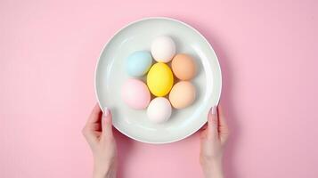 AI generated Two hands holding plate filled with colored Easter eggs on a soft pink background. Top view. Suitable for Easter event promotions and seasonal decor themes photo