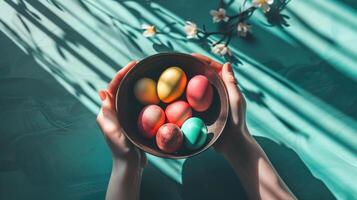 ai generado manos participación cuenco con vistoso pintado Pascua de Resurrección huevos, en contra un oscuro verde azul antecedentes con flores parte superior vista. con Copiar espacio. para Pascua de Resurrección promociones o temática de primavera culinario contenido foto