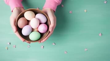 AI generated Hands holding bowl with colorful painted Easter eggs, against light green blue background. Top view. Banner with copy space. Suitable for Easter promotions or spring-themed photo