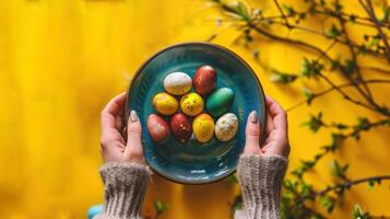 AI generated Colorful assortment of Easter eggs in a blue-green dish, cradled by hands with a bright yellow floral backdrop. Top view. Perfect for holiday-themed advertisements, DIY tutorials photo