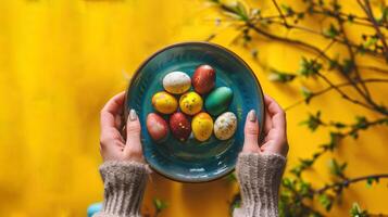 AI generated Colorful assortment of Easter eggs in a blue-green dish, cradled by hands with a bright yellow floral backdrop. Top view. Perfect for holiday-themed advertisements, DIY tutorials photo