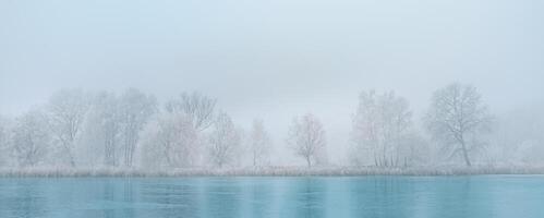 Winter landscape in soft blue tones with calm winter river lake, surrounded by frozen trees. Winter nature landscape with snowy frozen trees, beautiful frozen lake with reflection in water photo