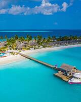 Beautiful aerial view of poolside and resort beach with wooden pier jetty. Luxurious tropical beach landscape, swimming, deck chairs and loungers, umbrellas. Tropical beach, aerial drone top view photo