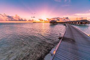 Sunset on Maldives island, luxury water villas resort and wooden pier. Beautiful sky and clouds and beach background for summer vacation holiday and travel concept photo