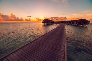 Sunset on Maldives island, luxury water villas resort and wooden pier. Beautiful sky and clouds and beach background for summer vacation holiday and travel concept photo