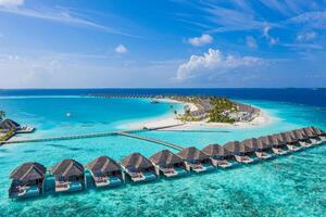 Aerial view of Maldives island, luxury water villas resort and wooden pier. Beautiful sky and ocean lagoon beach background. Summer vacation holiday and travel concept. Paradise aerial landscape pano photo