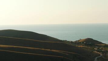 Aerial view of high green hills and blue sea on the background against the evening sky in summer. Amazing colorful landscape video