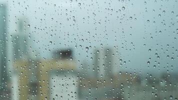 vicino su di un' bicchiere finestra su un' piovoso giorno con grande gocce su sfocato città ang grigio pesante cielo sfondo. azione filmato. trasparente acqua gocce su un' verticale bicchiere superficie. video