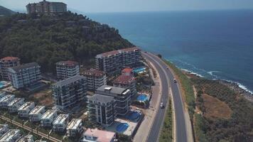 Aerial view of cars moving in the road near the sea and luxury hotels standing on the slope in warm summer day. Clip. Amazing summer resort video