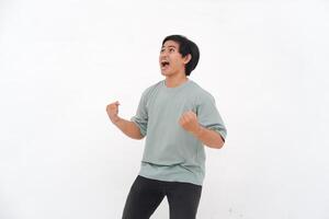 Young Asian man with an enthusiastic expression as if feeling victorious, depicting a sense of great satisfaction. photo