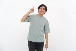 Excited Asian male employee wearing a tshirt pointing at the copy space above him, isolated by white background photo