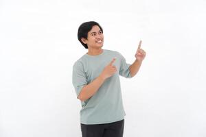 Excited Asian male employee wearing a tshirt pointing at the copy space above him, isolated by white background photo