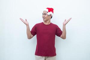 Young Asian man wearing a Santa Claus hat smiling, shock and pointing to her side isolated by white background for visual communication photo