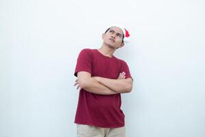 Young Asian man wearing a Santa Claus hat crossing his arms while smiling, shock and laughing with a white background for visual communication photo