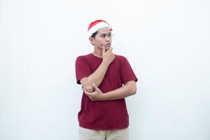 joven asiático hombre vistiendo un Papa Noel claus sombrero sonriente, conmoción y señalando a su lado aislado por blanco antecedentes para visual comunicación foto