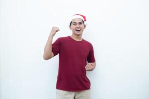 Young Asian man wearing a Santa Claus hat gripping both hands with enthusiasm and anger isolated by a white background for visual communication photo